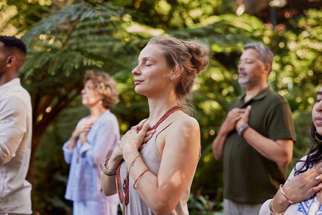 Group of people standing outdoors with hands on their hearts, practicing mindfulness in a wellness retreat