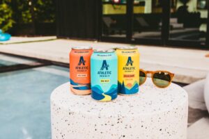 three cans of Athletic Brewing Co.'s line of nonalcoholic drinks on a concrete pillar near a pool
