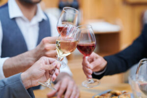 three men in work attire toast glasses of wine while drinking with colleagues