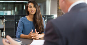 man interviewing a woman with long brown hair and a blue shirt in a bid to achieve the company goal of hiring employees with emotional intelligence