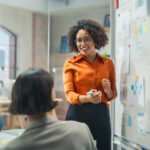 woman standing in front of a white board talks with coworkers in a conference room about inclusive marketing