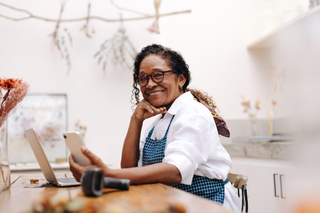 Mature Black business owner looking at the best self employed retirement plans on her phone and computer