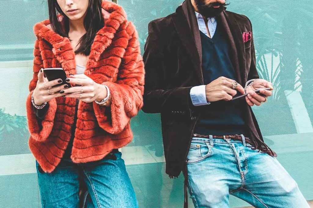 two young influencers in expensive clothing looking down at their phones and taking part in the de-influencing trend