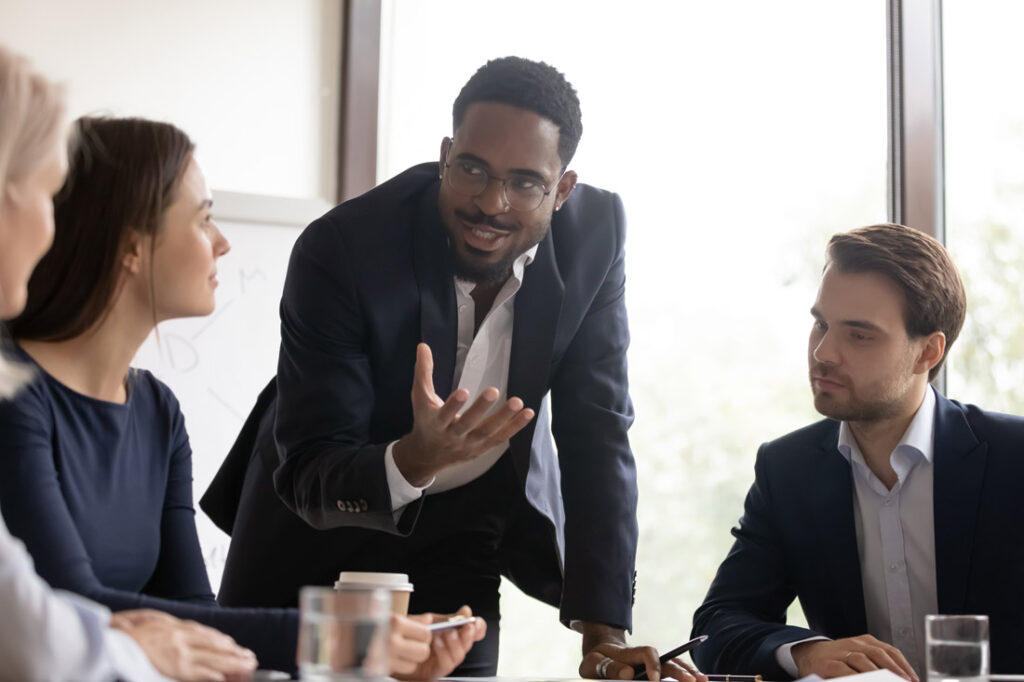 Photograph of a Black man leading his colleagues through a presentation, speaking with his hands to demonstrate emotional intelligence in leadership