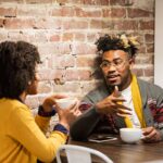 a young man and women sit across from each other talking in a coffee shop with strong personality type compatibility