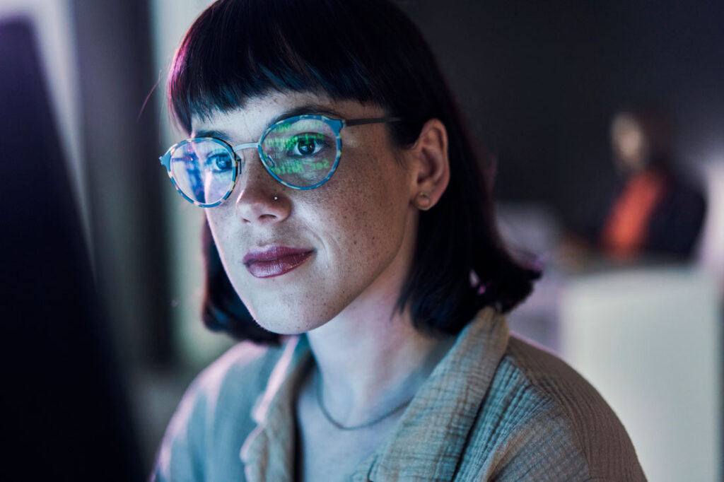 short-haired woman fixing AI bias with computer screen blue light reflecting in her glasses