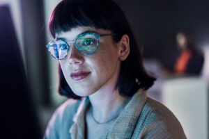 short-haired woman fixing AI bias with computer screen blue light reflecting in her glasses