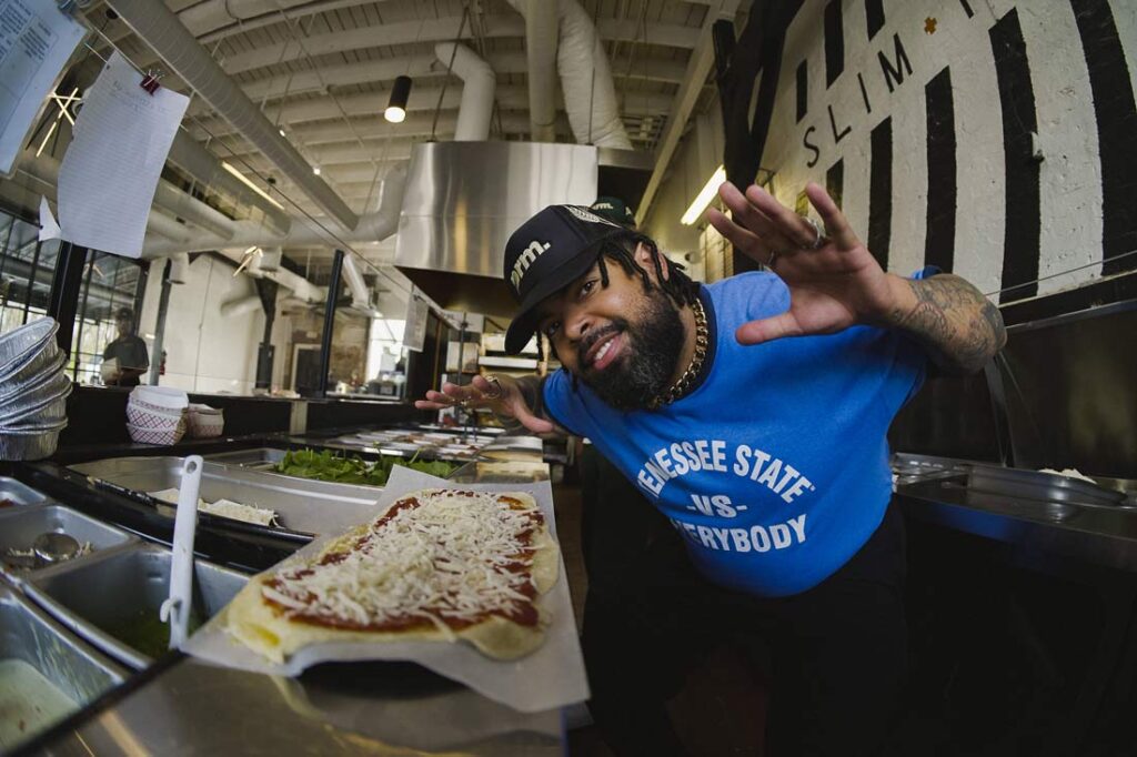 Slim & Husky's co-founder leaning over a flatbread pizza with jazz hands