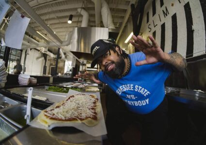 Slim & Husky's co-founder leaning over a flatbread pizza with jazz hands