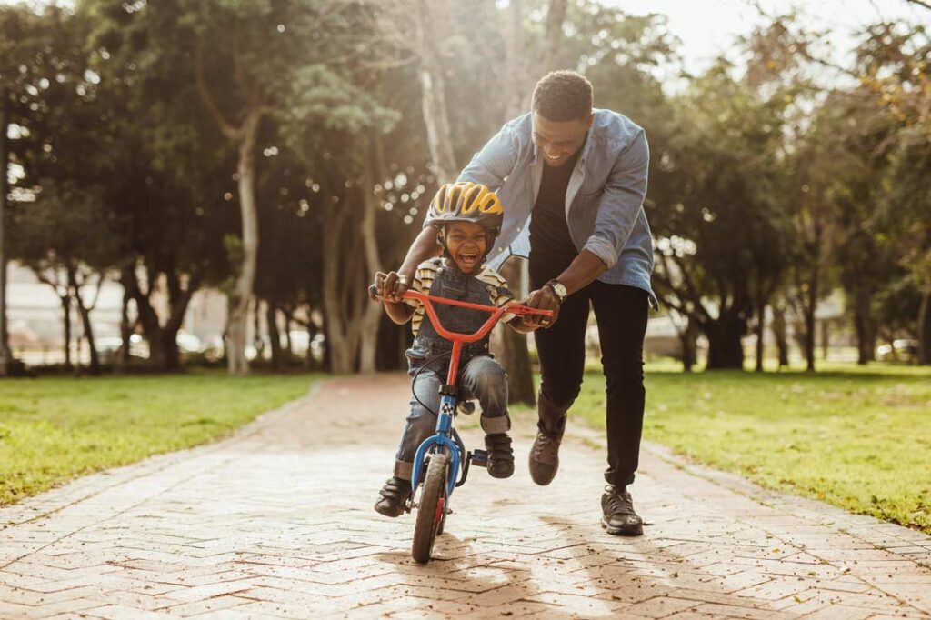 happy dad helping his excited young son learn to ride a bike during one of their 18 summers together