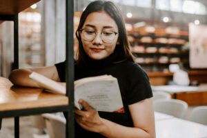 young woman in a library reading a book to build confidence