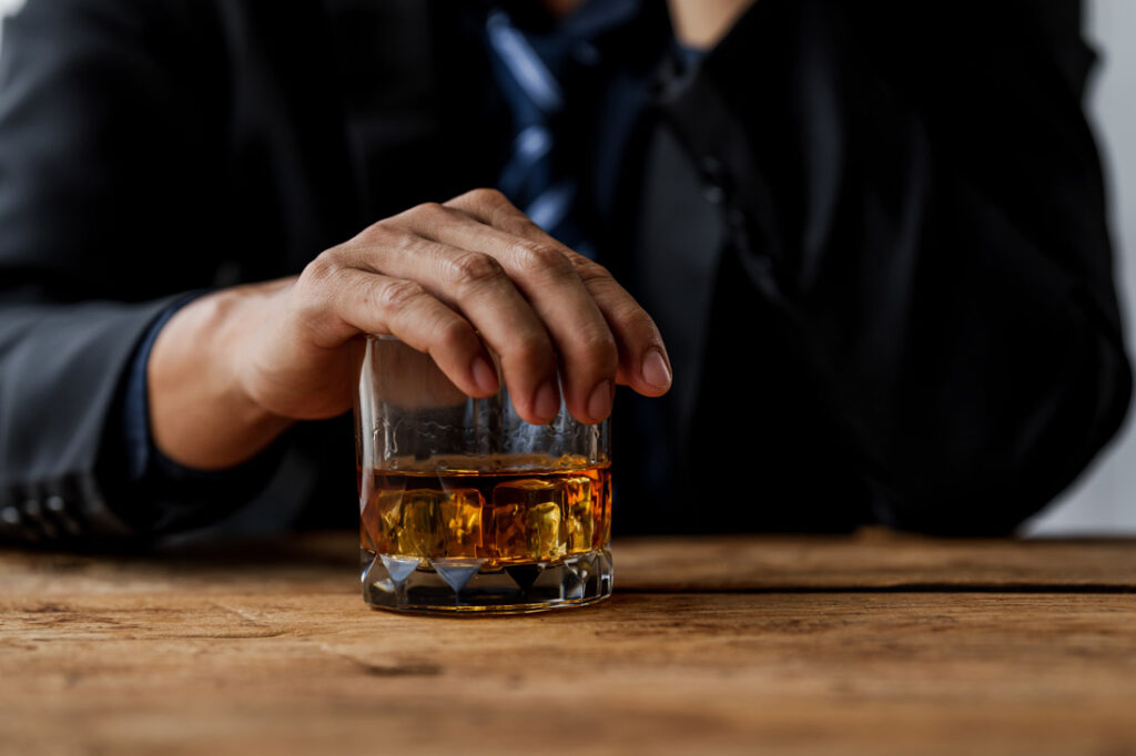 Close up photograph of a man in a suit with his hand over a glass of whiskey to symbolize quitting drinking