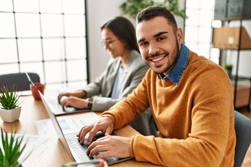 Two business workers sitting at a desk in the office, smiling because they have employee autonomy