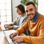 Two business workers sitting at a desk in the office, smiling because they have employee autonomy
