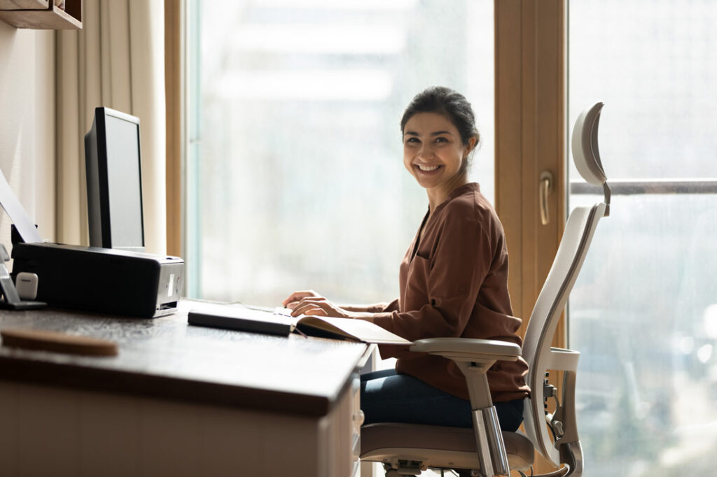 An Indian woman smiling and working at her ergonomic home office