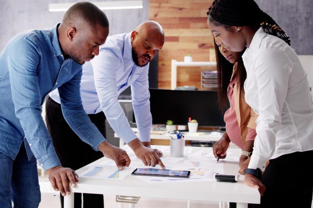 Photograph of 4 Black business people leaning over a conference table and studying a marketing swot analysis