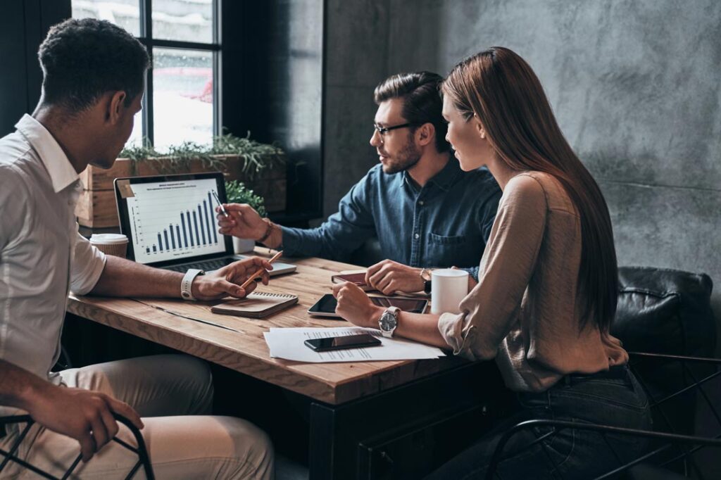 Photograph of three coworkers performing a swot analysis at a desk in front of a laptop