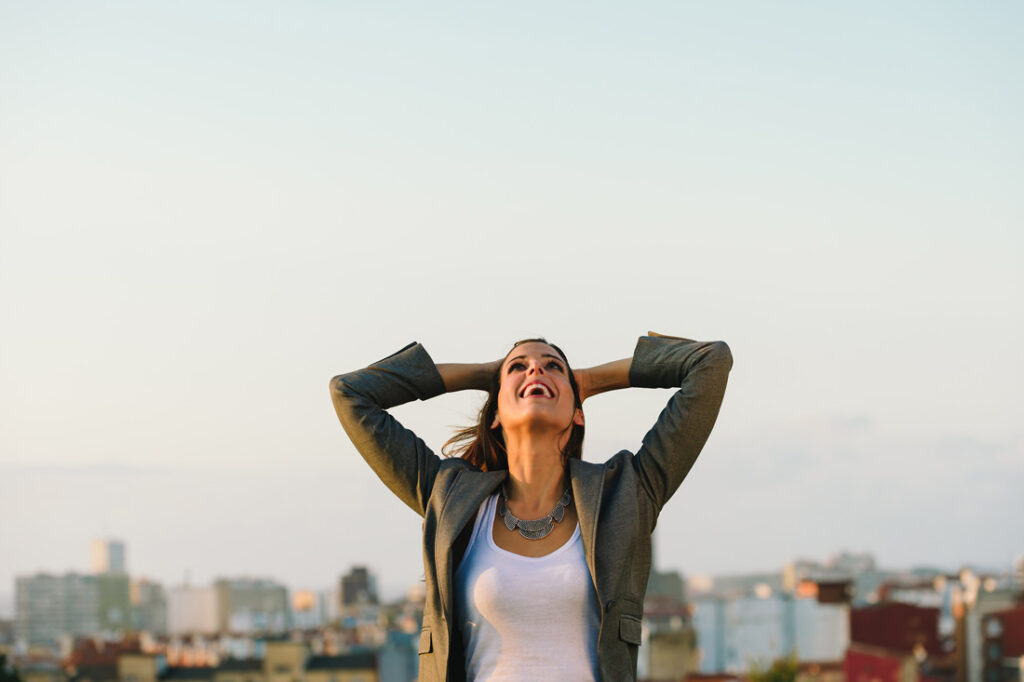 A business woman on a rooftop with the city in the background embracing failure and looking up towards the sky