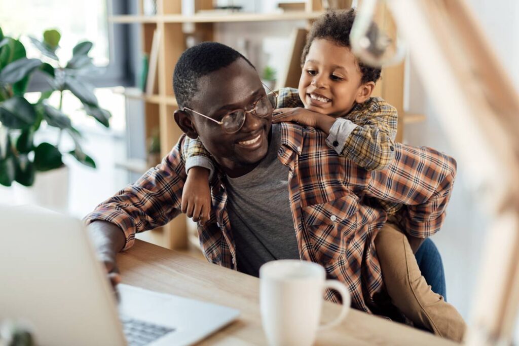 Black father with his young son in front of his computer learning how to negotiate flexible working arrangements