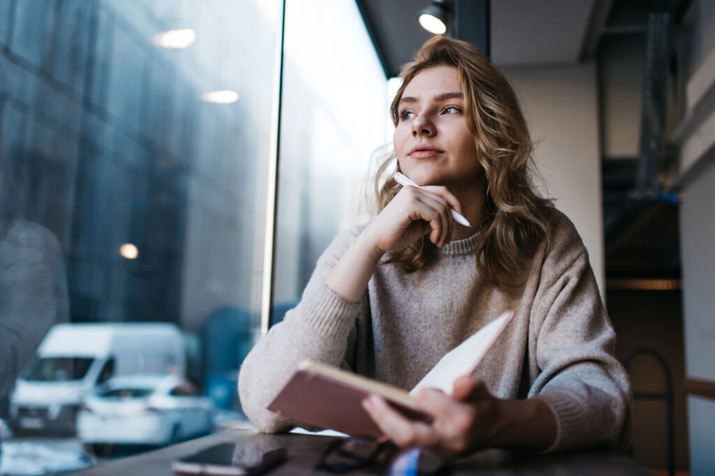 Blonde woman looking out a window pensively showing how to stay motivated at work during difficult times