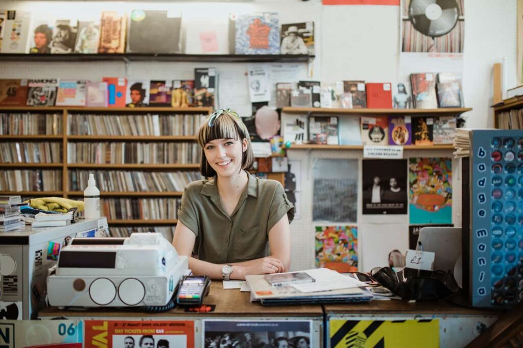 young woman standing behind the counter of a record shop getting ready for small business saturday 2023