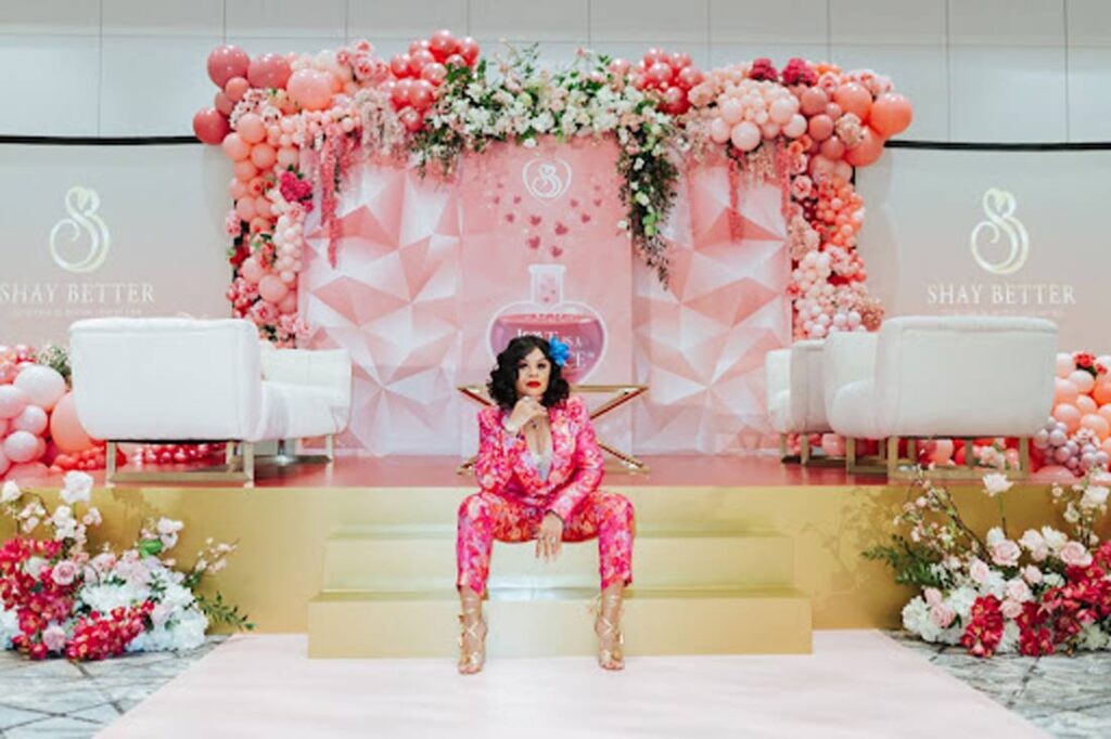Shay 'Your Love Diva' Levister sitting on golden steps surrounded by pink flowers
