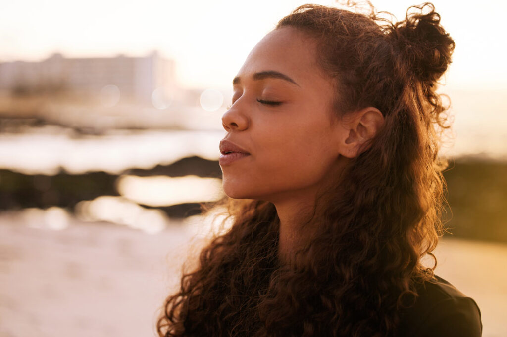 Woman at the beach with her eyes closed learning how to practice gratitude