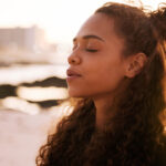 Woman at the beach with her eyes closed learning how to practice gratitude
