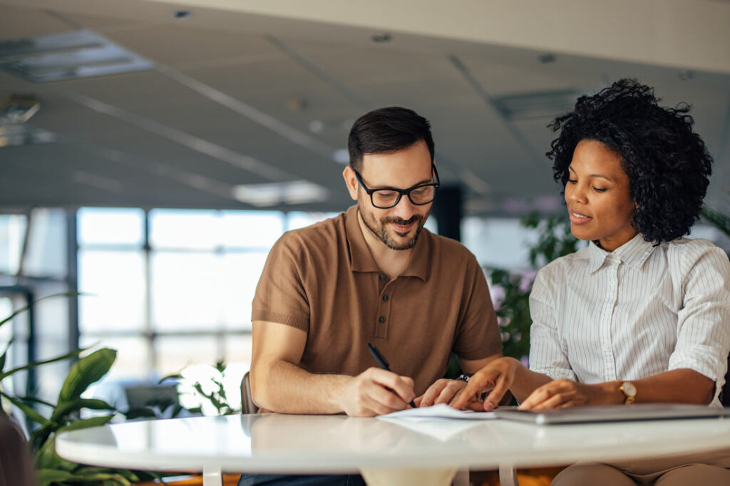 A Black female professional helping her white male colleague with how to list soft skills on resume