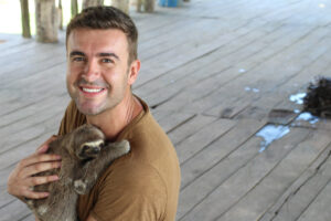 Man holding a sloth and smiling at a volunteer abroad program