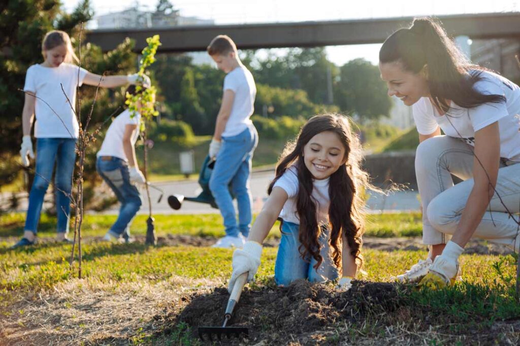 Young girl planting trees with her mother enjoying volunteer opportunities for kids