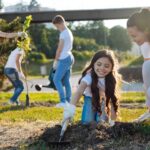 Young girl planting trees with her mother enjoying volunteer opportunities for kids