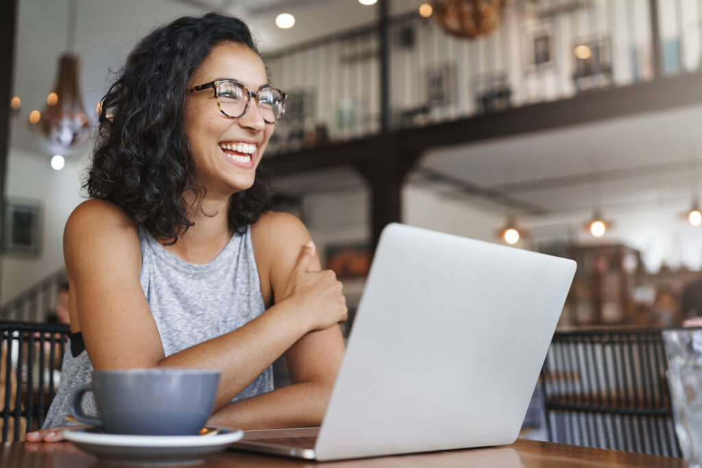 Smiling woman working on her computer in a cafe learning how to make money with AI