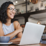 Smiling woman working on her computer in a cafe learning how to make money with AI