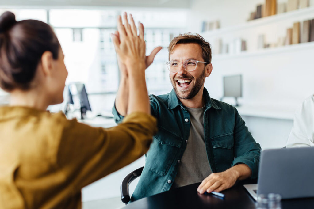 Two colleagues high fiving and smiling because they understand the 5 languages of appreciation in the workplace