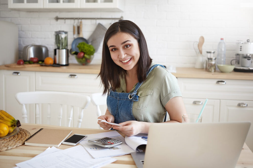 Woman sitting in her kitchen planning her short term financial goals and smiling
