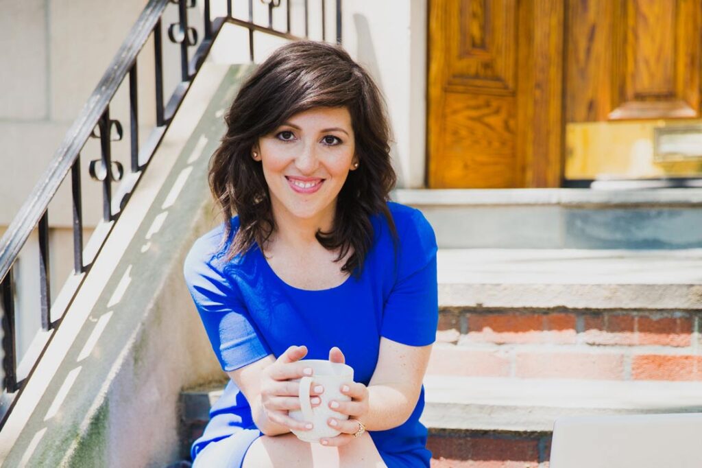 Stella Grizont, author of the Work Happiness Method, sitting on a stoop with a coffee mug in her hands