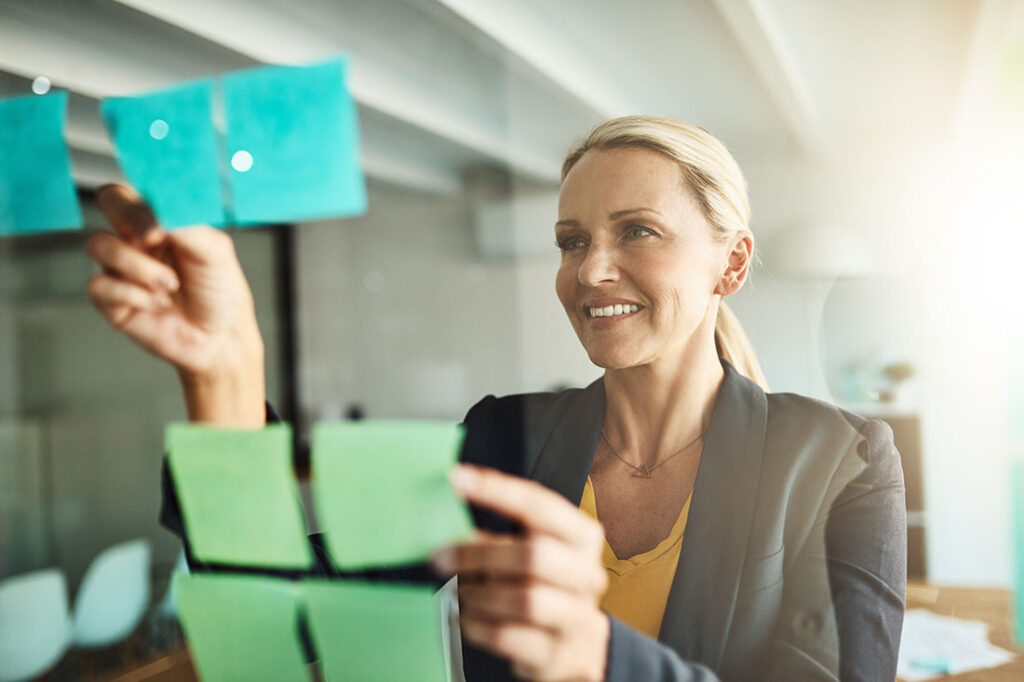 woman putting notes on glass board at office for vision board