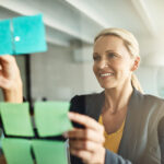 woman putting notes on glass board at office for vision board