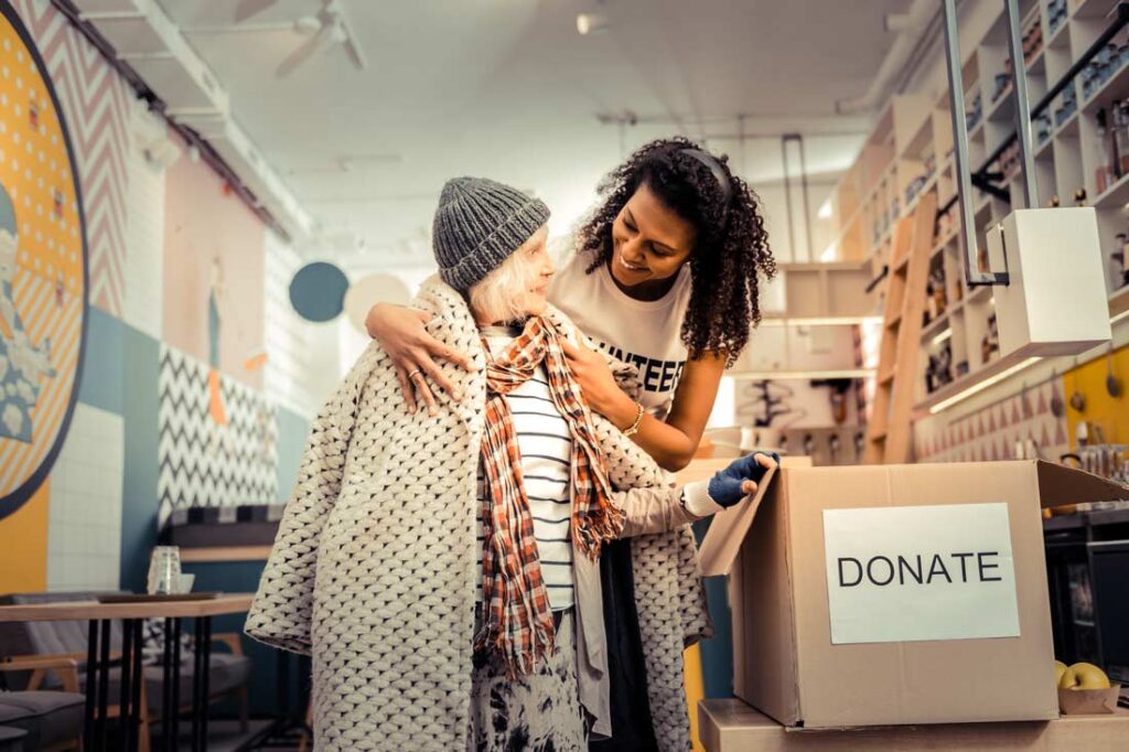 Volunteer putting a jacket on an elderly woman in need learning how volunteering helps mental health