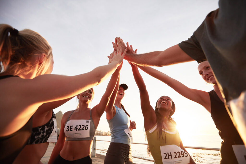 Group of runners high fiving on the beach at sunset learning the importance of marathon running and community