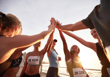 Group of runners high fiving on the beach at sunset learning the importance of marathon running and community