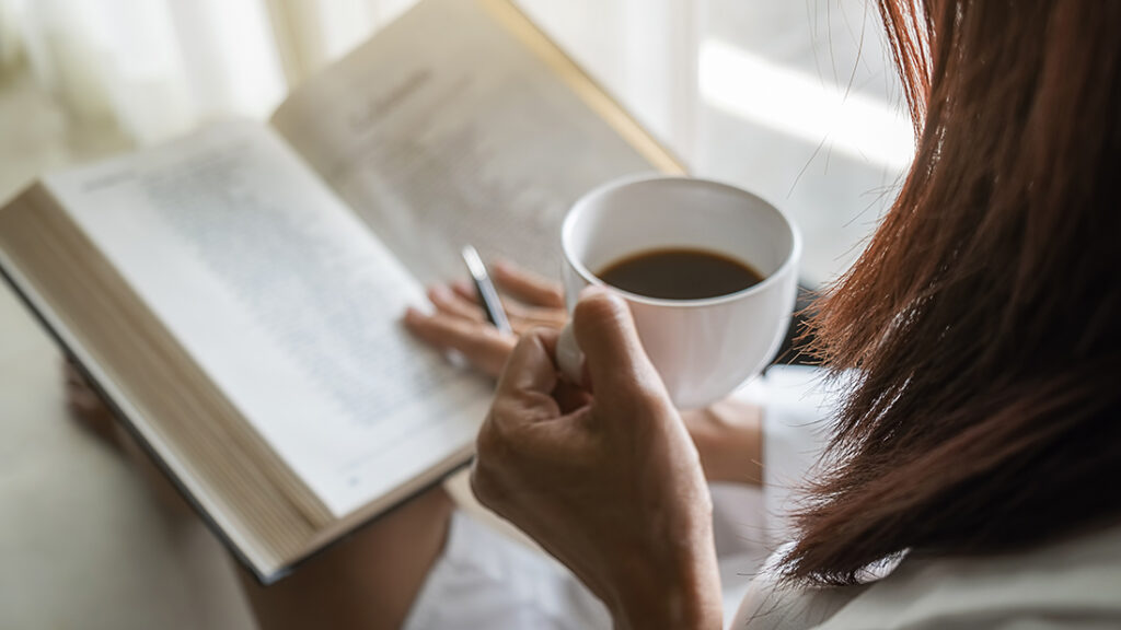 Woman reading a book while holding a cup of coffee