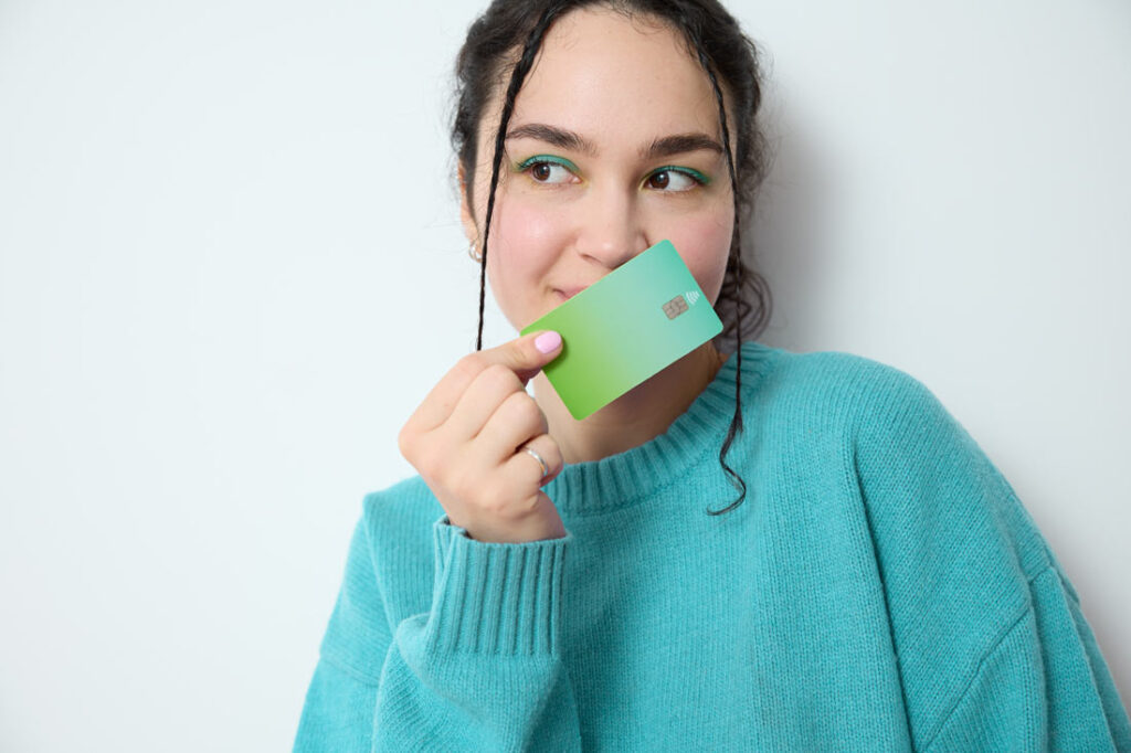 20 year old woman smiling behind her credit card exemplifying biggest financial mistakes that young adults make