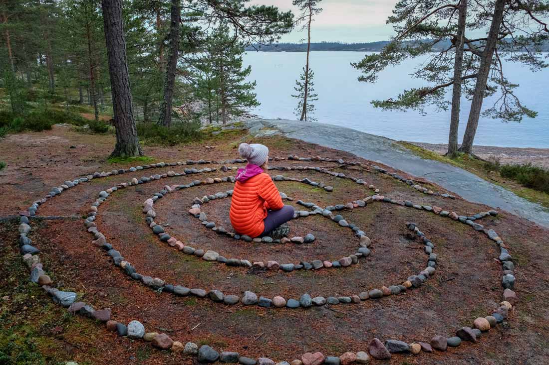 Woman sitting in the middle of a meditation labyrinth overlooking a lake she built in her backyard