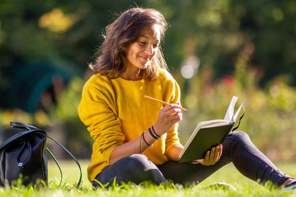Woman outside writing in her journal and smiling while learning How to identify areas for personal development