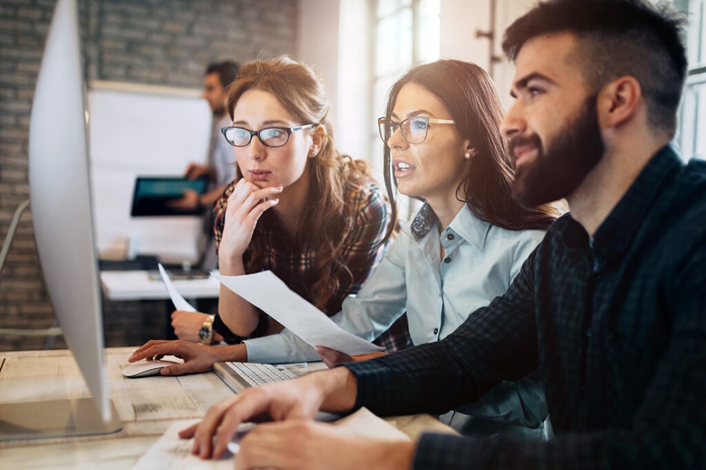 Three business professionals gathered around a computer