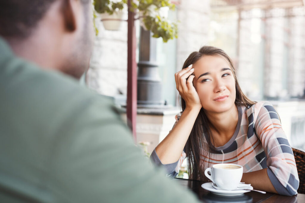 Woman with empathy fatigue trying to pay attention to a conversation over coffee but failing