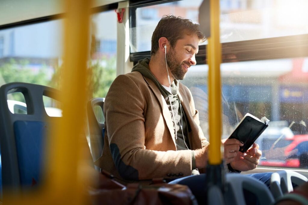 A man commuting, listening to music and reading a book, enjoying his liminal space