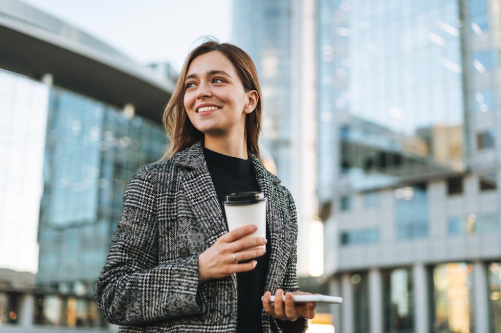 Young business woman standing in front of office building smiling because she understands the difference between professional vs personal development
